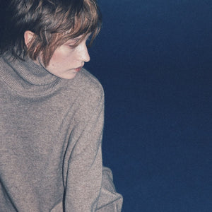 Woman wearing a brown cashmere turtleneck sweater against a dark blue background