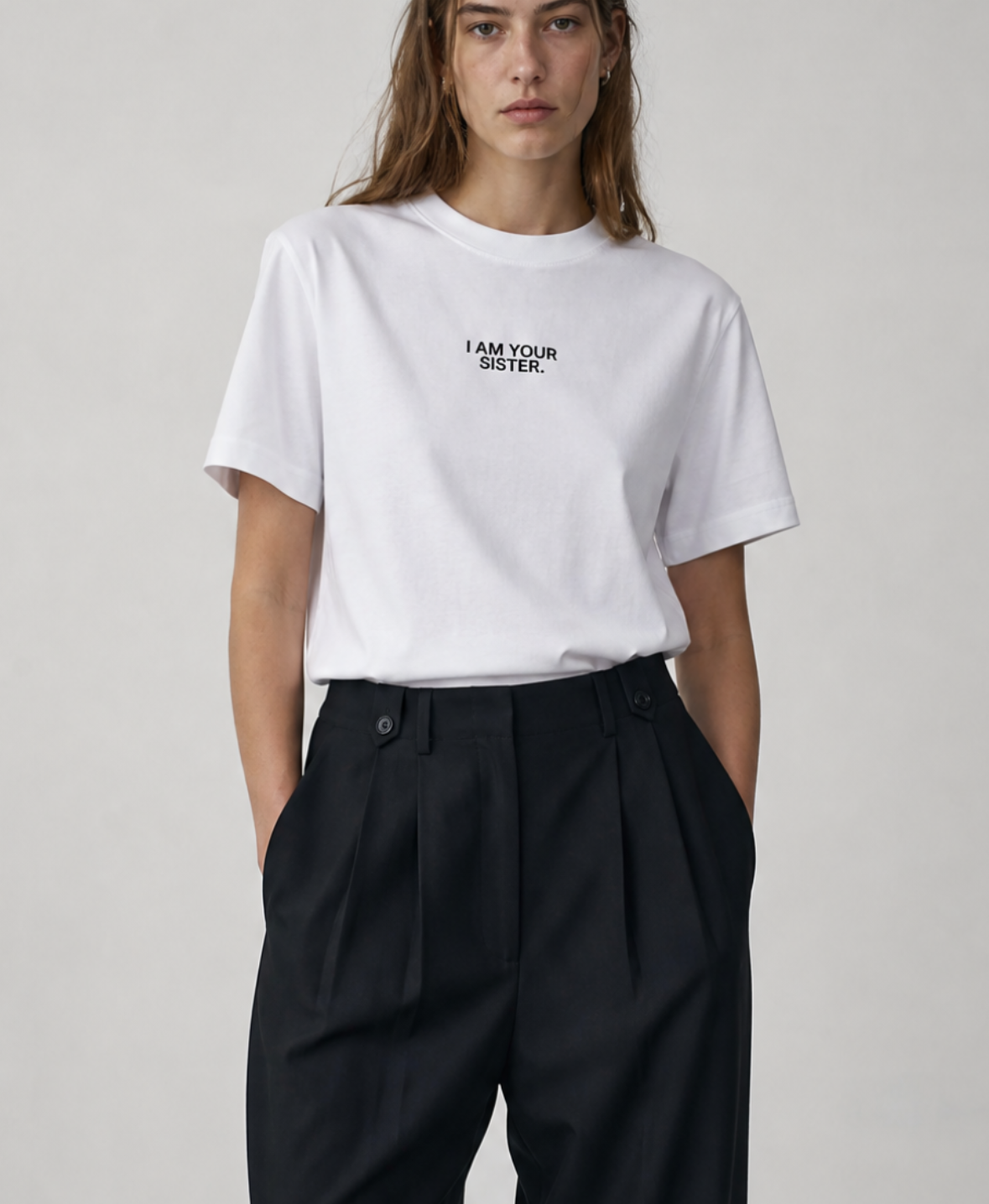 Person wearing a white I am your sister t-shirt and black pants on a plain background