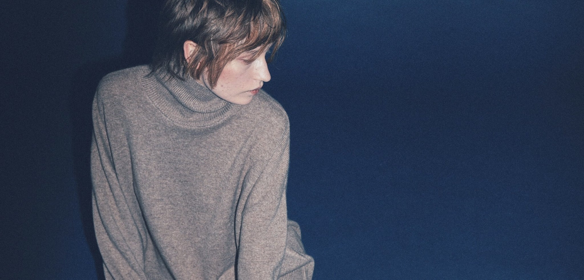 Woman wearing a brown cashmere turtleneck sweater against a dark blue background