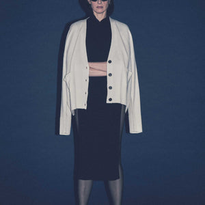 Woman wearing a luxury cream colored cashmere  cardigan over a black outfit against a dark blue background