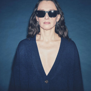 A woman wearing a navy v-neck cardigan with front button-up closure and front pockets, against a dark background.