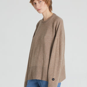 A female model wearing a brown cashmere crew neck long-sleeve sweater and blue jeans.