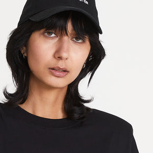 A woman wearing a black baseball cap with an embroidered 'I AM YOUR SISTER' logo on the front.