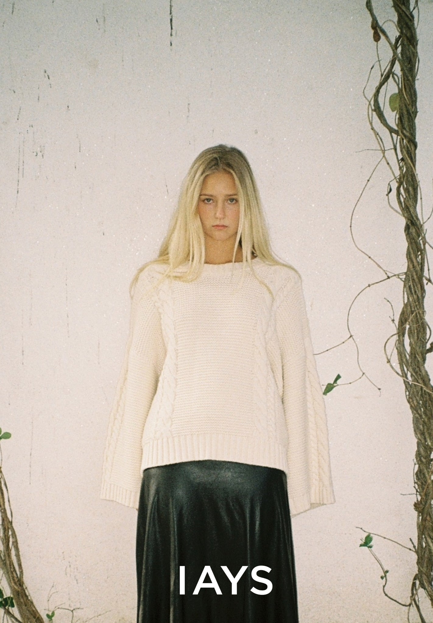 Woman wearing a white sweater and black skirt with 'IAYS' branding against a white background.