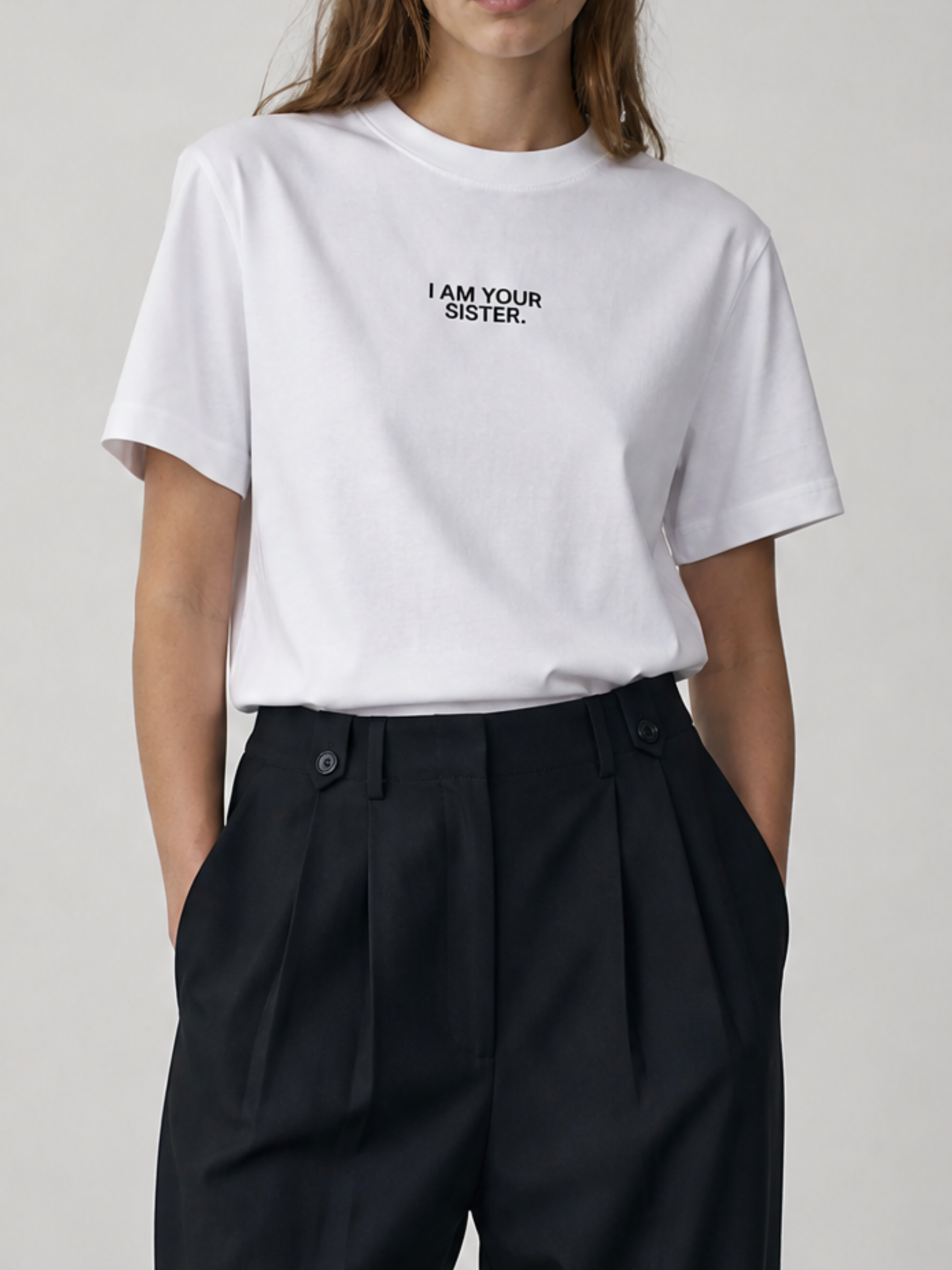 Person wearing a white t-shirt with 'I AM YOUR SISTER.' text on a plain background