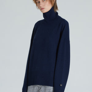 A navy turtleneck cashmere sweater with ribbed trims, displayed on a woman with a neutral expression.