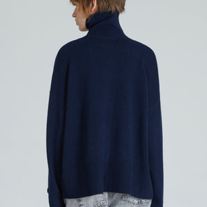 Back of navy turtleneck cashmere sweater with ribbed trims, displayed on a woman with grey jeans.