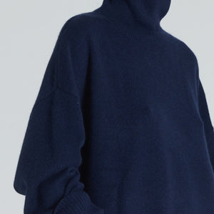 Closeup of a navy turtleneck cashmere sweater with ribbed trims, displayed on a woman with a neutral expression.