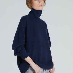 A woman wearing a navy cashmere turtleneck sweater with ribbed trims and a relaxed silhouette.