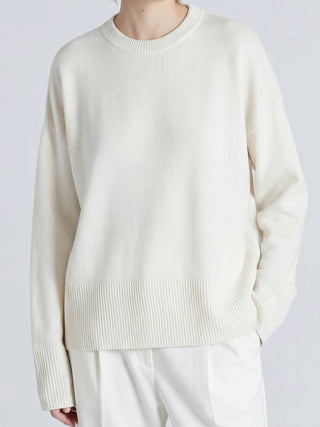Person wearing a cream sweater and white pants on a light gray background